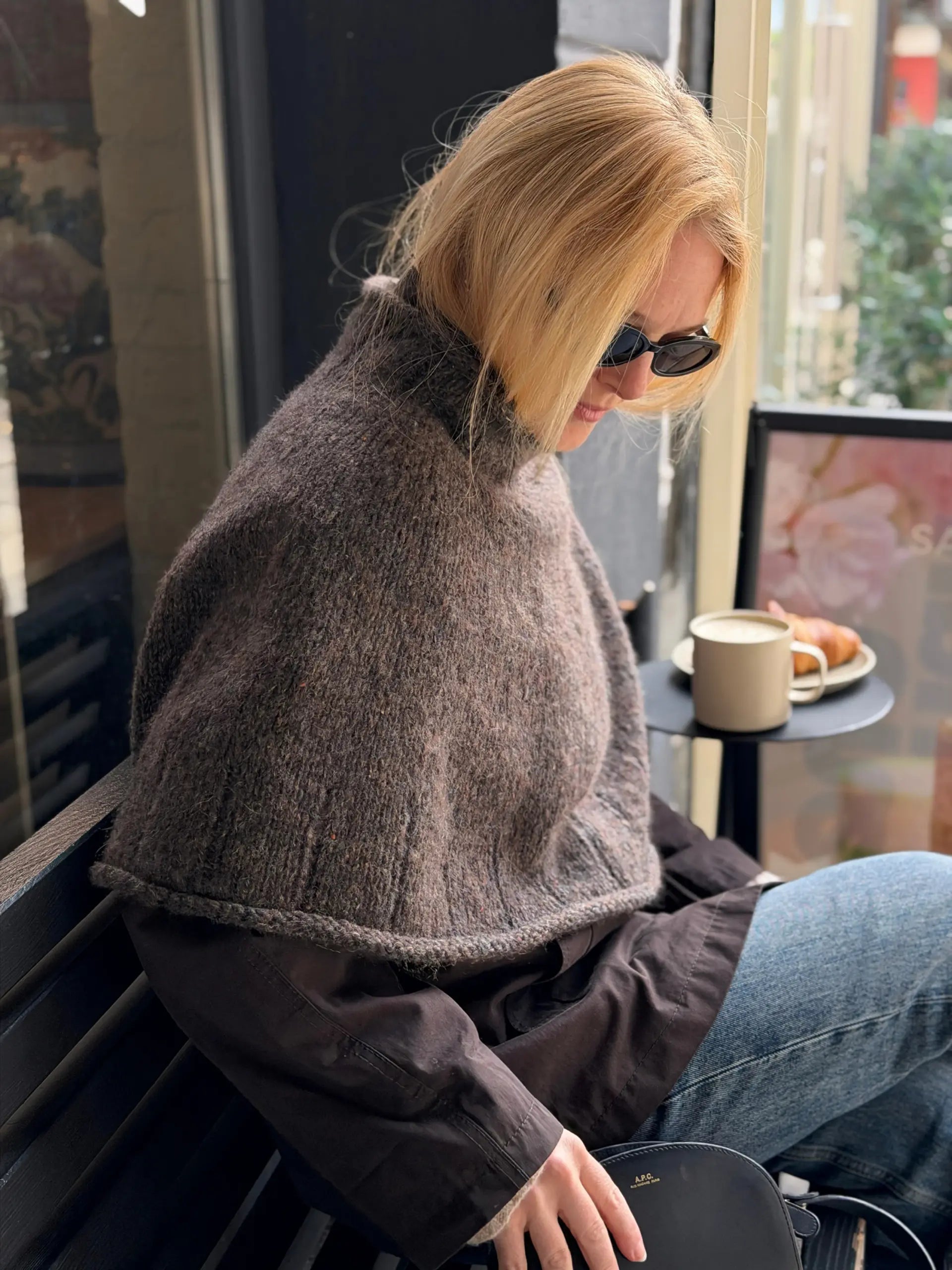 Frau trägt die Heia Tweedcape von Rauma, gestrickt aus Fivel 214 und Alpakka Lin Tweed 21798, mit breiten Rippenkanten
