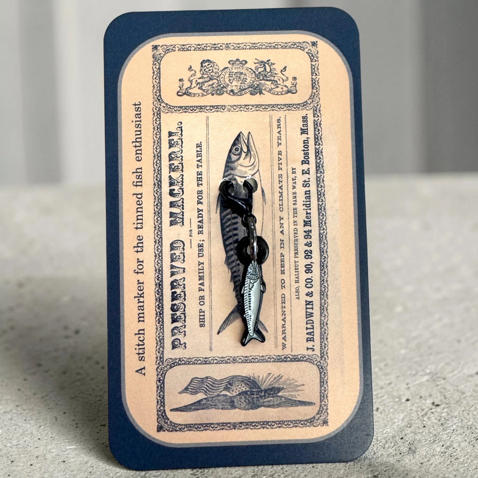 Firefly Notes Maschenmarkierer Preserved Mackerel aus Metall und Emaille, silberne Makrele mit schwarzem Hakenverschluss auf dunkelblauer Karte mit Vintage-Fischdosenetikett