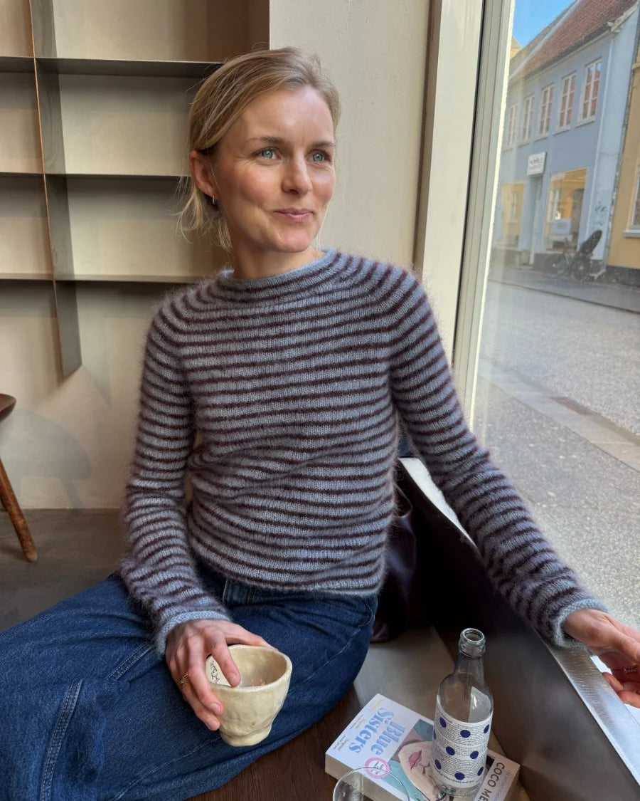 Frau trägt die Frankie Blouse von PetiteKnit, ein figurnaher Pullover in Blau mit bordeauxfarbenen Streifen aus Isager Silk Mohair