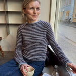 Frau trägt die Frankie Blouse von PetiteKnit, ein figurnaher Pullover in Blau mit bordeauxfarbenen Streifen aus Isager Silk Mohair